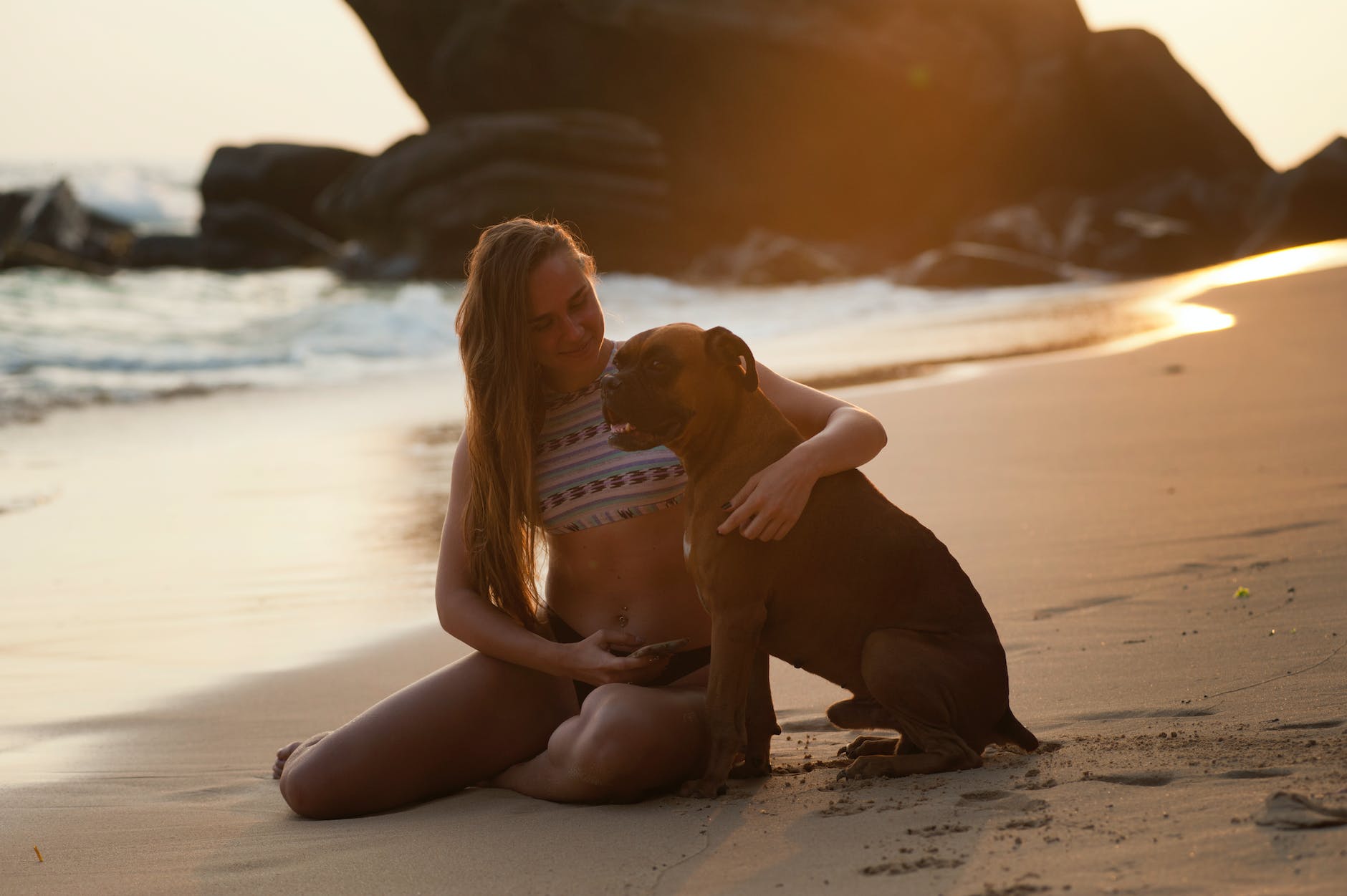 woman holding boxer dog on beach shore