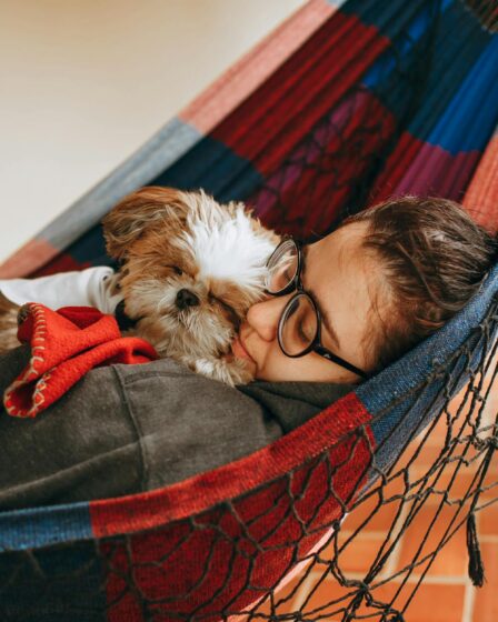 a woman is laying in a hammock with her dog